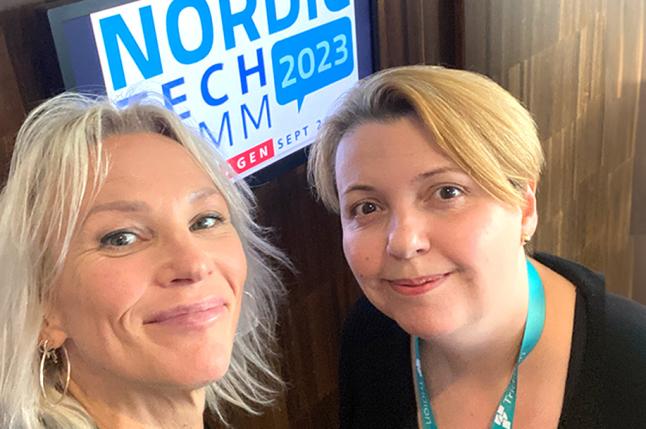 Två kvinnor framför en skylt som det står Nordic Techkomm på.