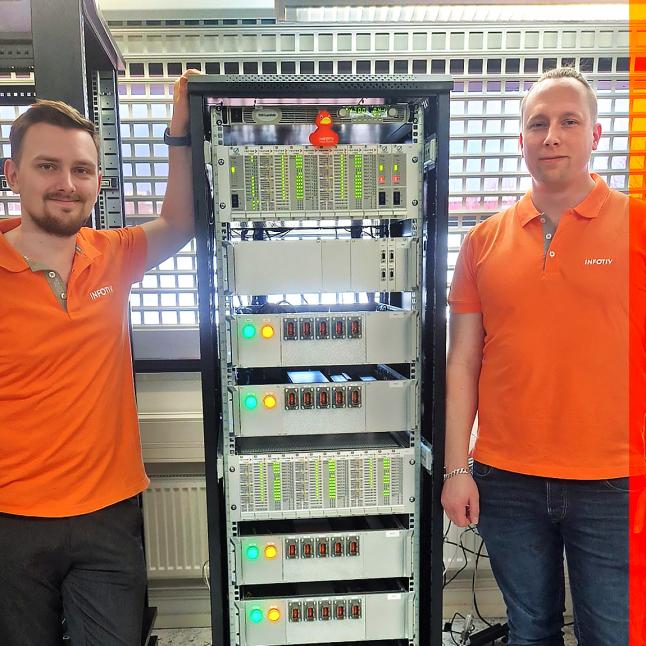 Två män i orange piketröjor står på varsin sida om en HIL-rigg.
